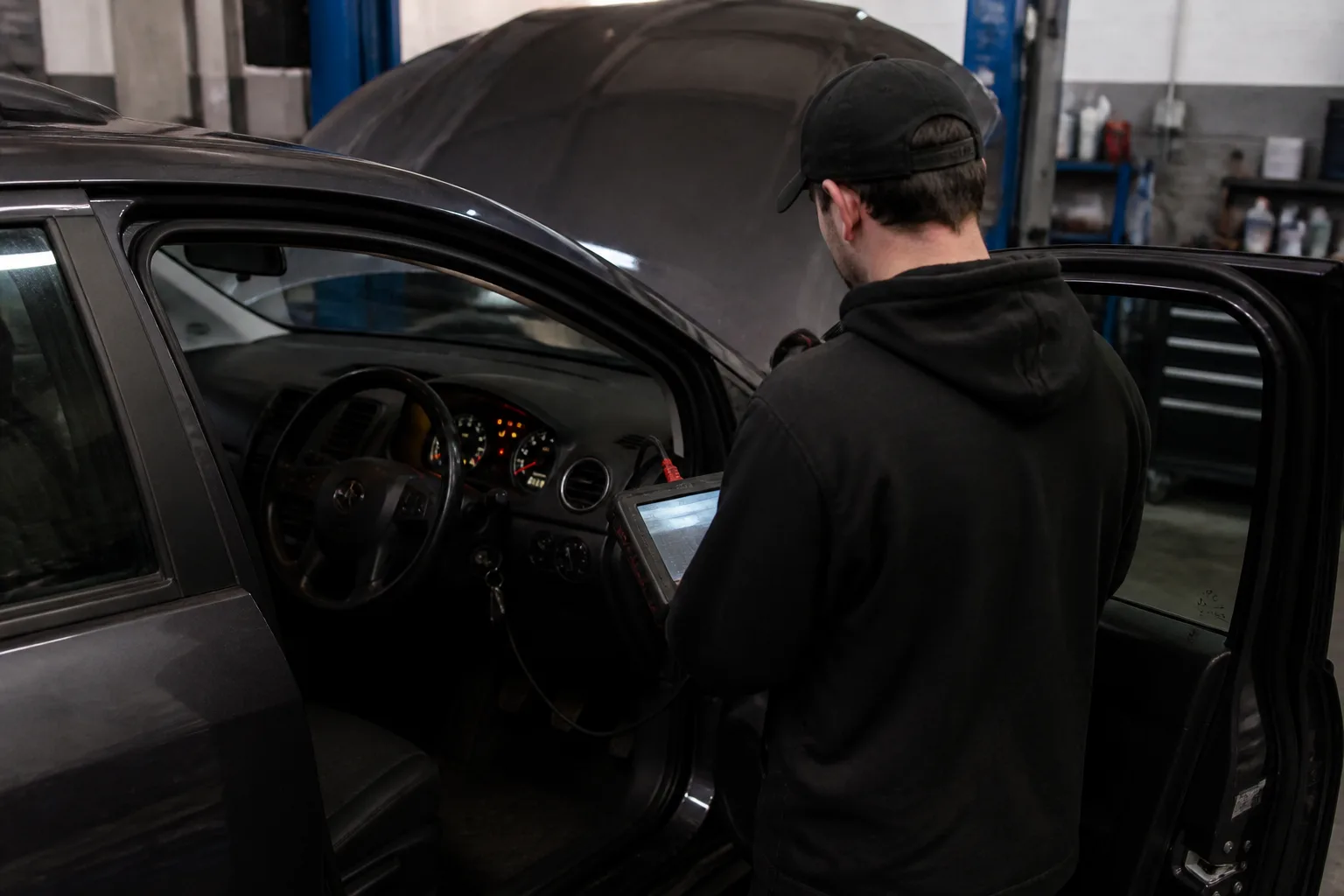 Mechanic using a diagnostic tool on a UK car showing several dashboard warning lights in an independent garage
