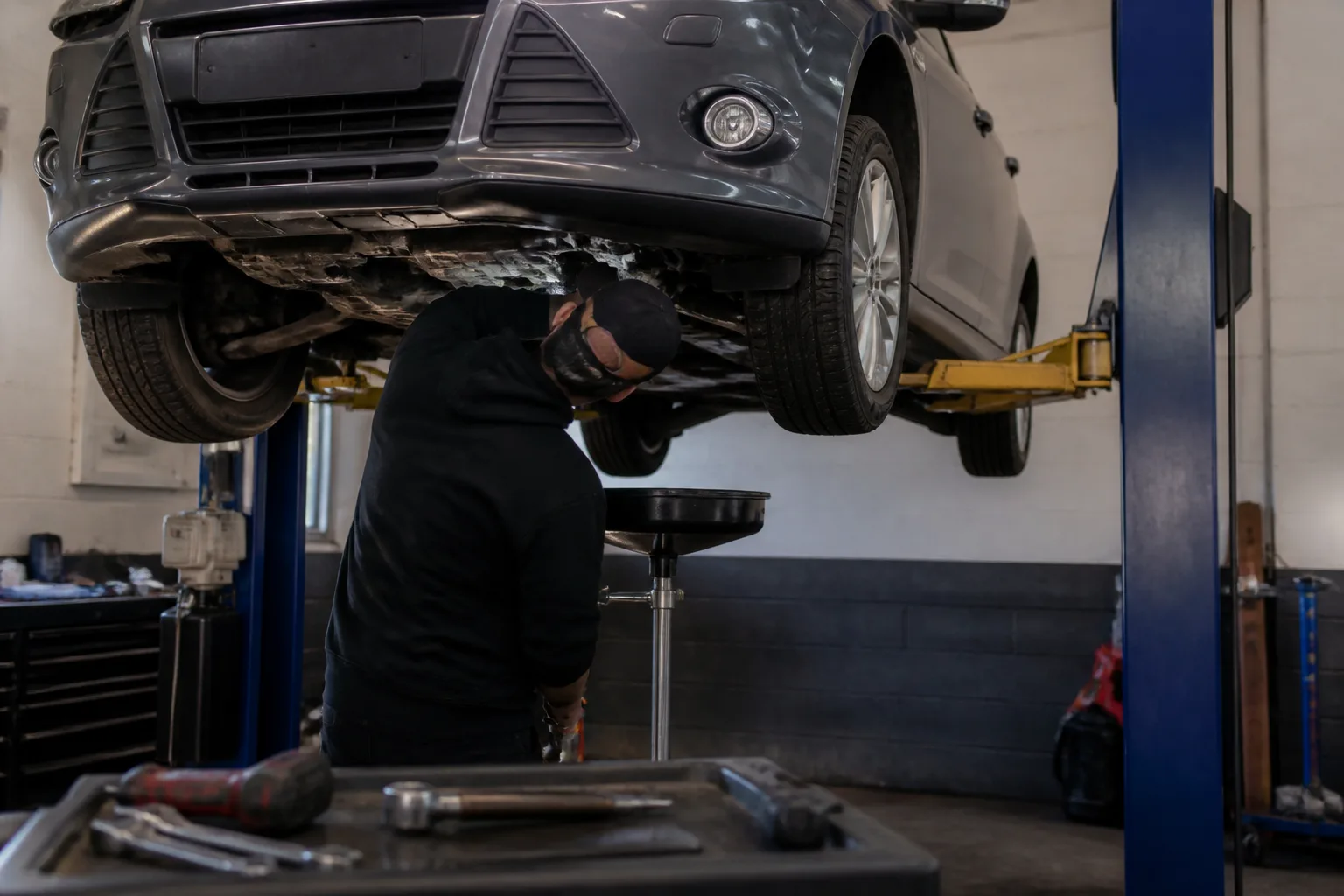 Mechanic safely inspecting the underside of a UK car for a possible engine oil leak in an independent garage